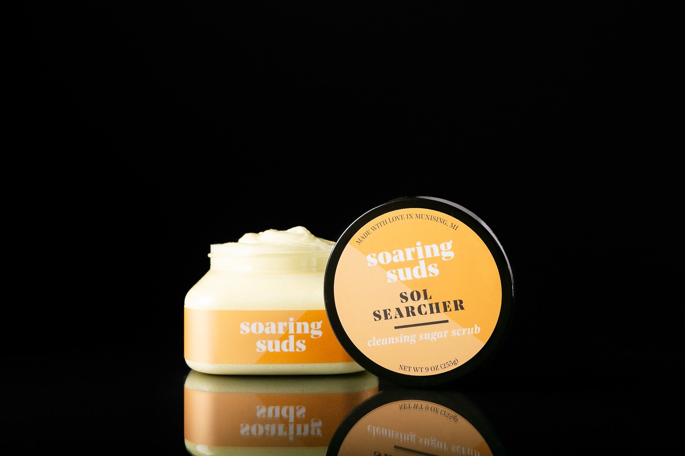 Sol Searcher Cleansing Sugar Scrub in a clear jar, showcasing its creamy texture and vibrant color, surrounded by fresh lemons and grapefruit.