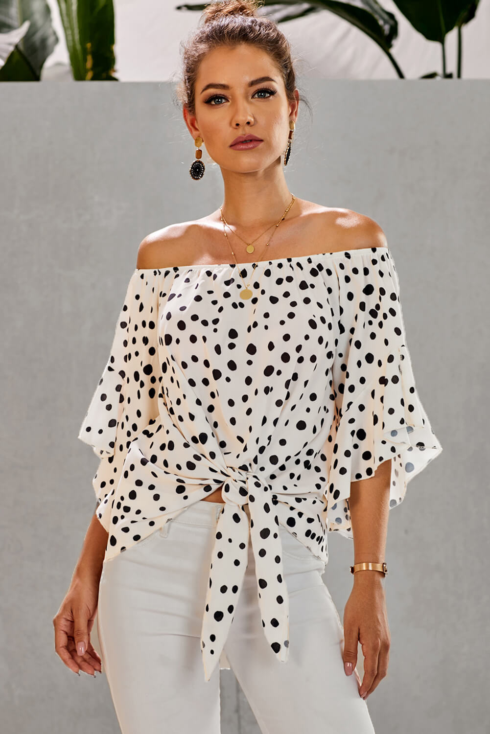 A stylish white polka dot off shoulder top with 3/4 bell sleeves and a front tie knot, perfect for casual outings.