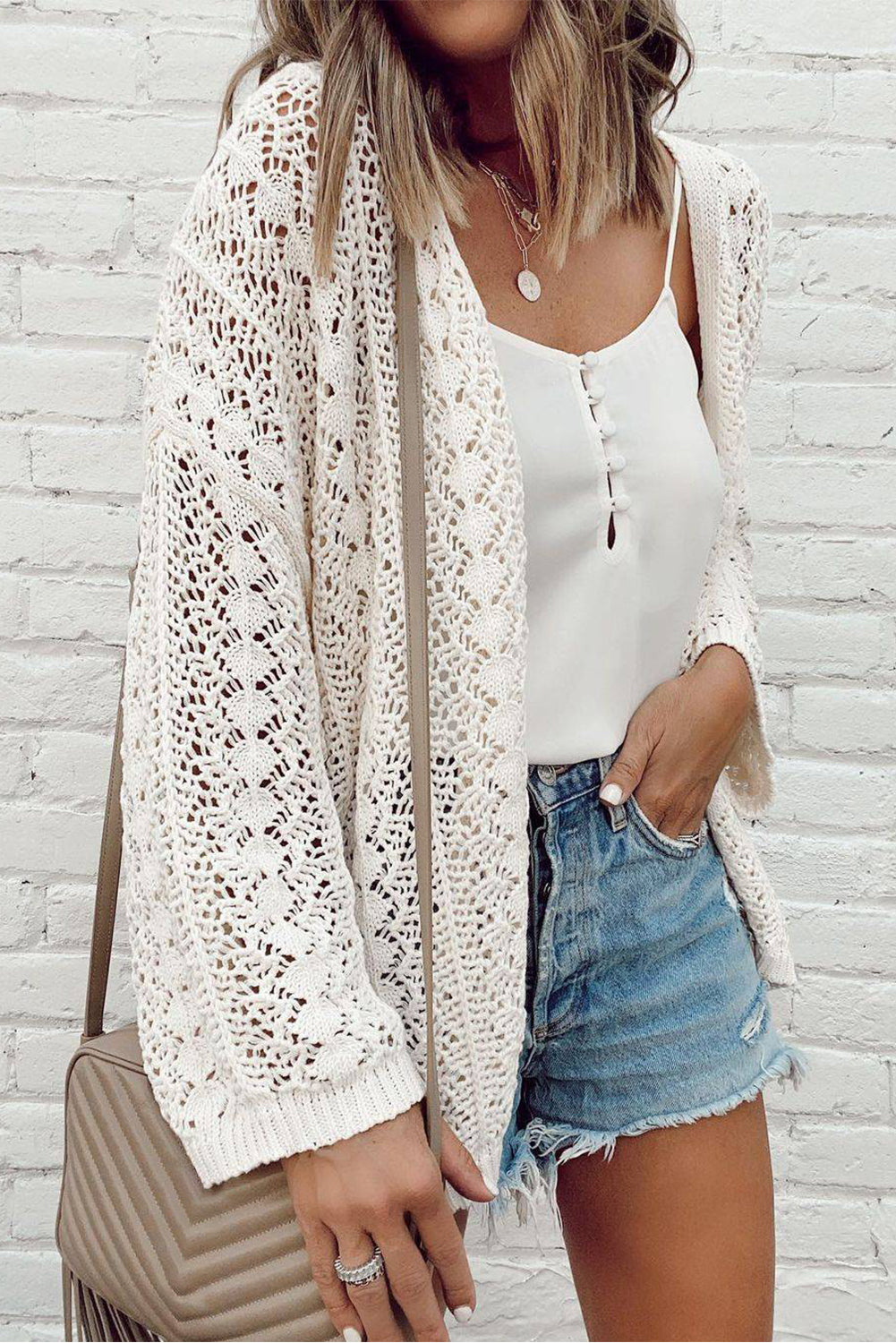 A stylish white cardigan featuring a hollow-out knit design and drop shoulder style, perfect for layering over outfits.