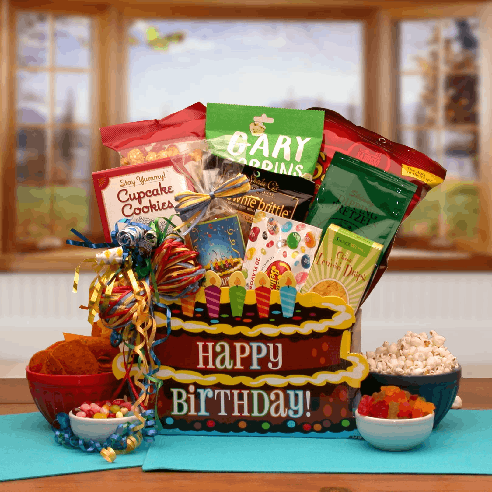 You Take The Cake Birthday Gift Box filled with assorted treats like gummi bears, popcorn, and cookies, beautifully wrapped with a raffia bow.