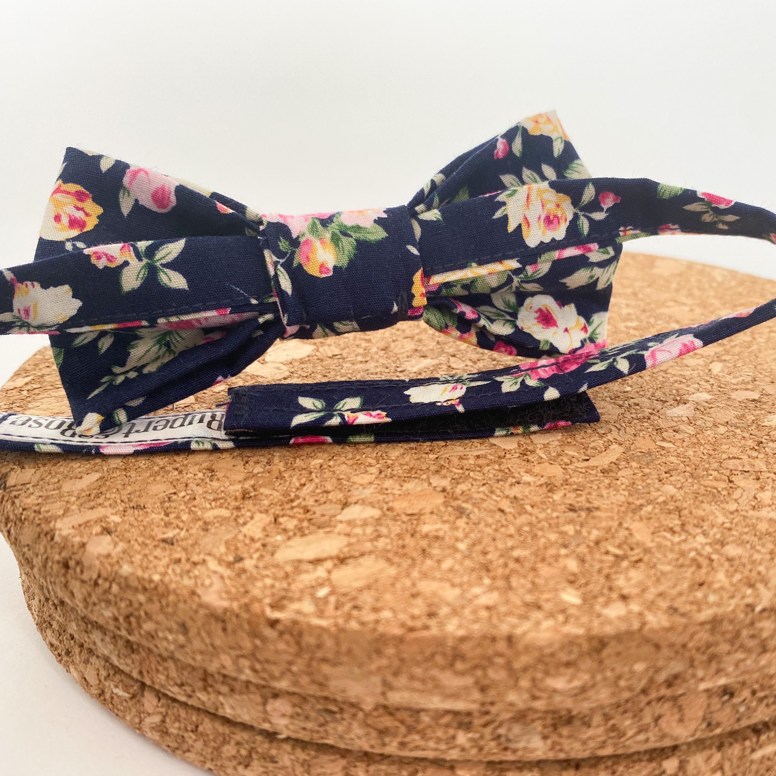 JAMESON Boys Bow Tie featuring pink and yellow roses on a navy background, handmade in England with velcro fastening.