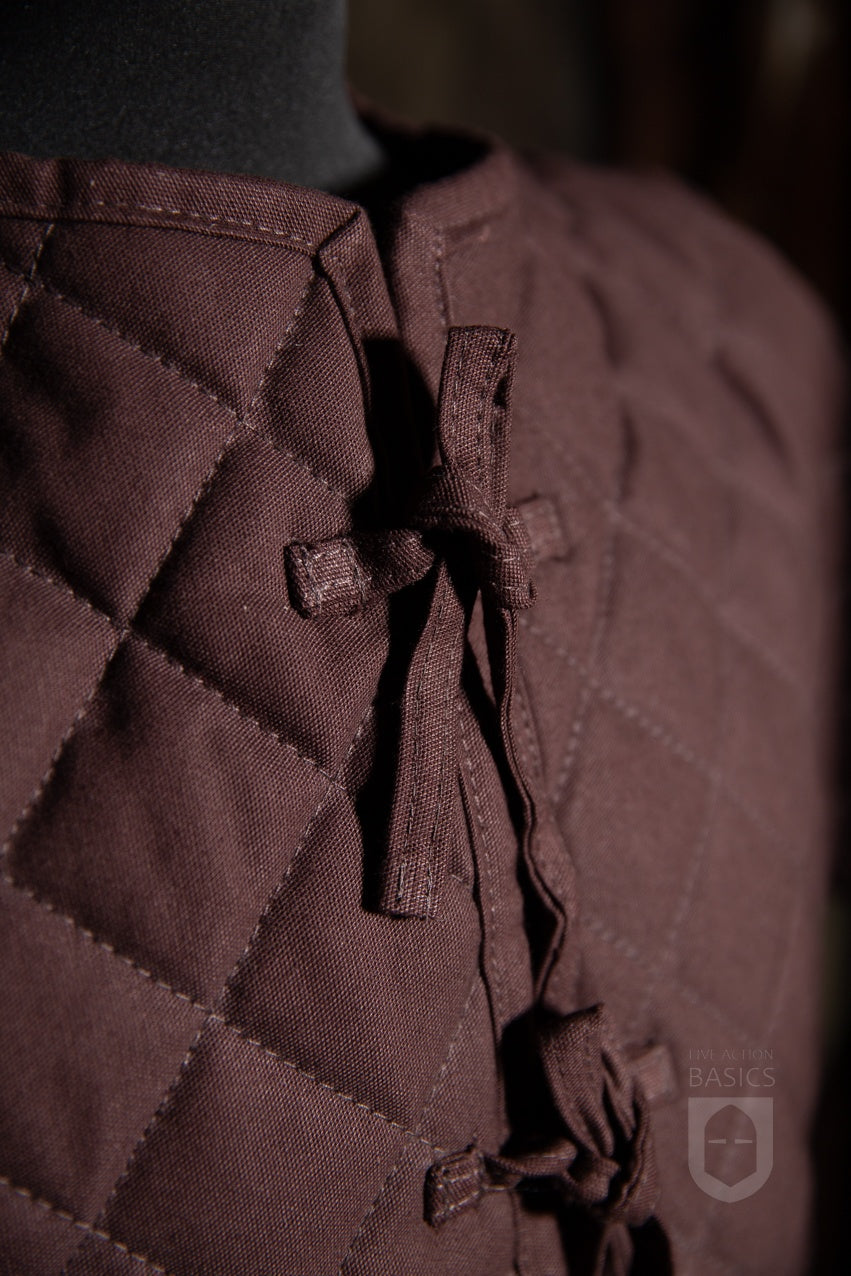 Basic Gambeson in brown color, featuring a quilted diamond design and front ribbons for tying.