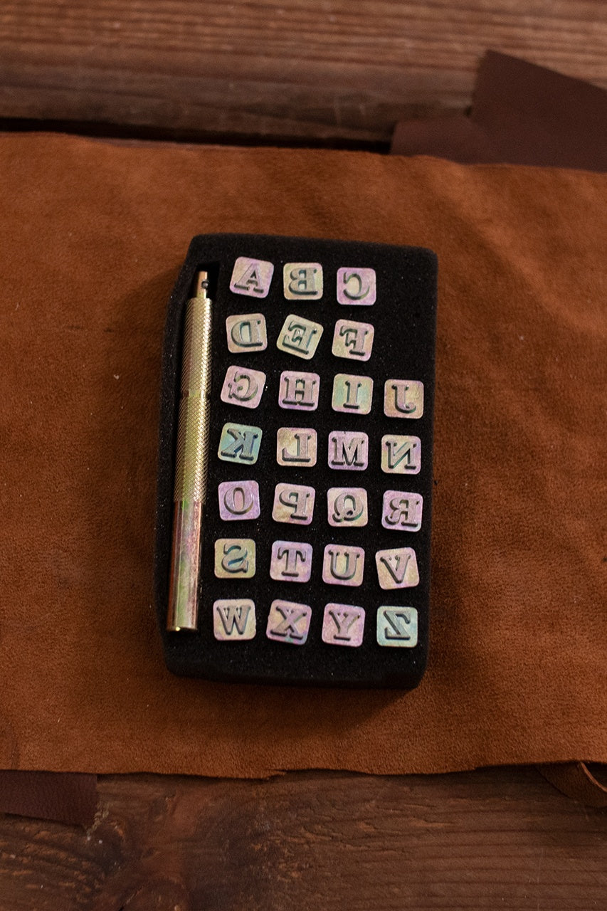 Embossing Tool Set featuring 26 iron alphabet stamps and a handle, ideal for personalizing leather crafts.