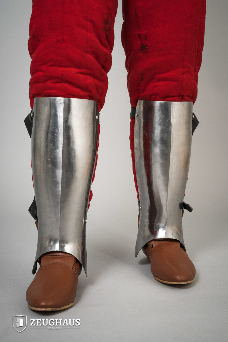 Polished 14th-century greaves designed for lower leg protection, featuring an anatomical shape for comfort.