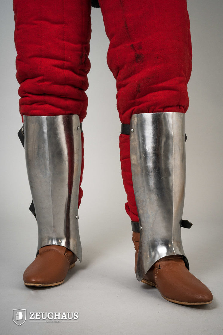 Polished 14th-century greaves designed for lower leg protection, featuring an anatomical shape for comfort.