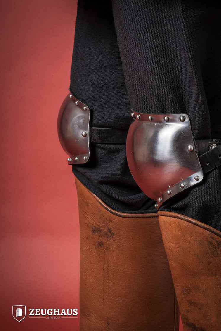 A pair of 14th century knee caps made from 1.6mm polished steel, featuring leather straps for secure attachment.