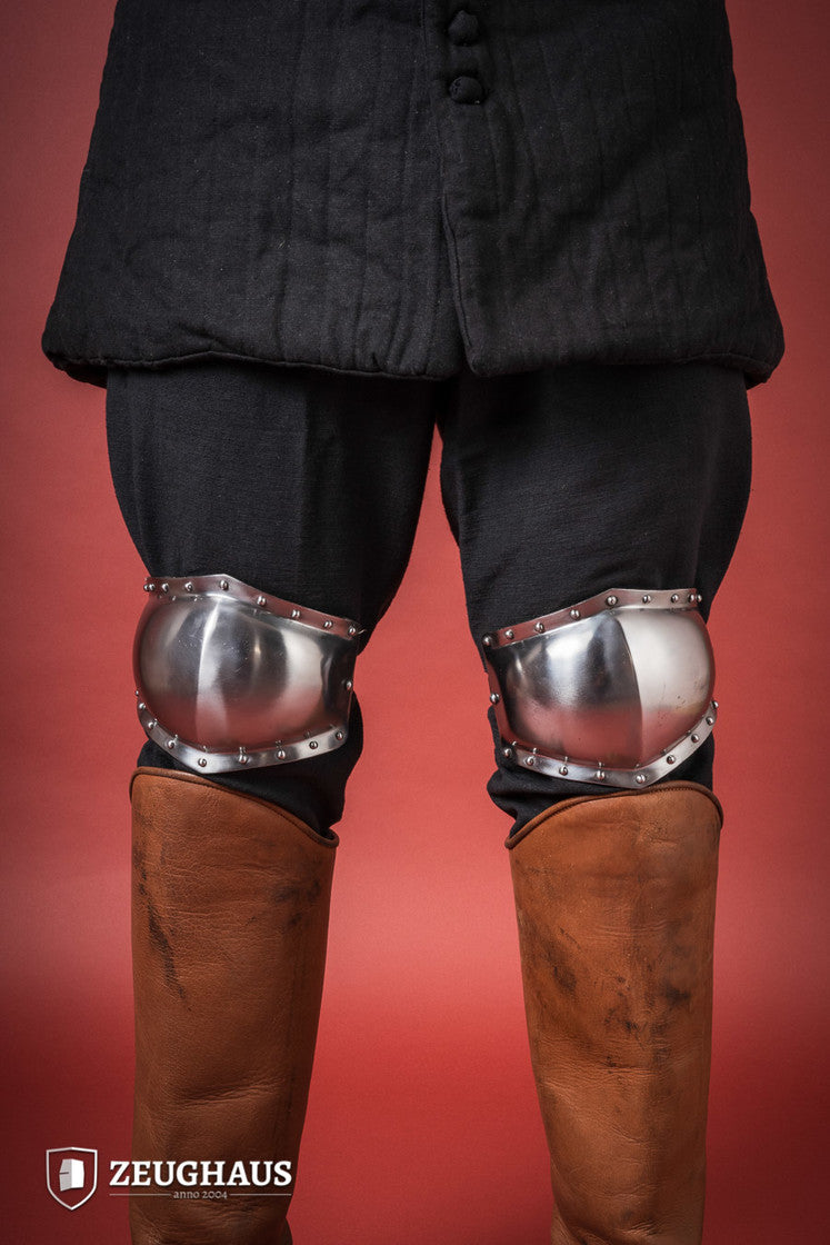 A pair of 14th century knee caps made from 1.6mm polished steel, featuring leather straps for secure attachment.