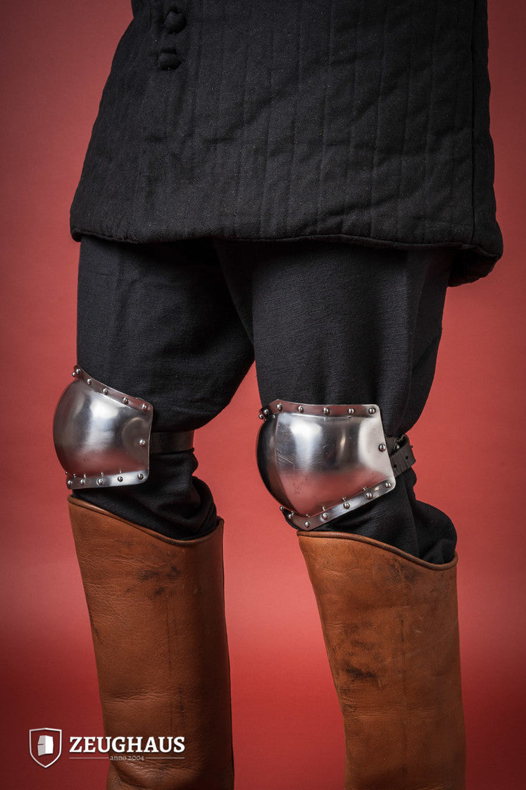 A pair of 14th century knee caps made from 1.6mm polished steel, featuring leather straps for secure attachment.