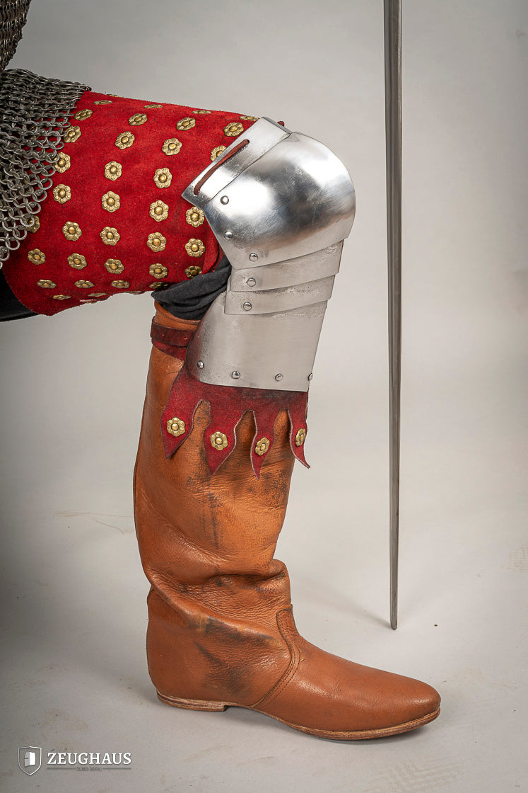 Splinted Leg Armour made of red suede leather with metal bands, showcasing intricate craftsmanship and historical design.