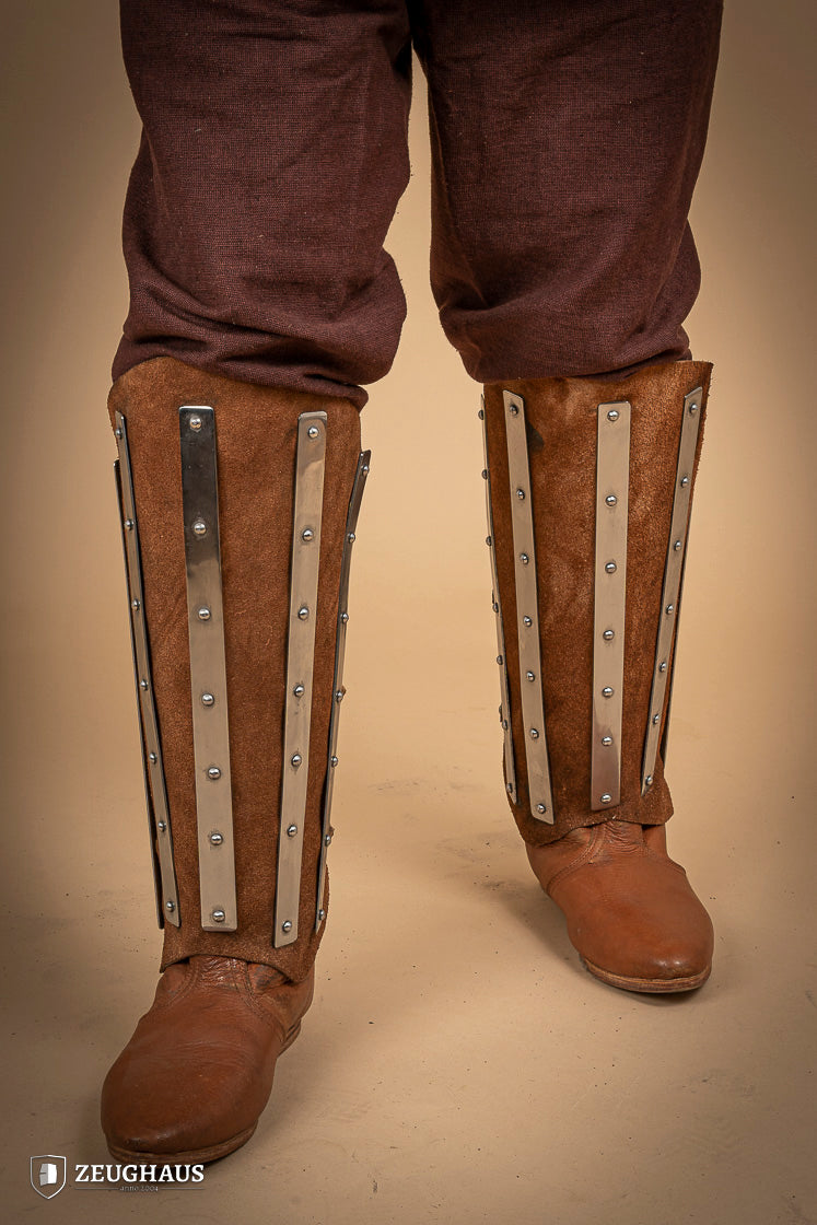 Brown suede leather greaves with riveted metal bands, showcasing a unique three-piece design for shin protection.