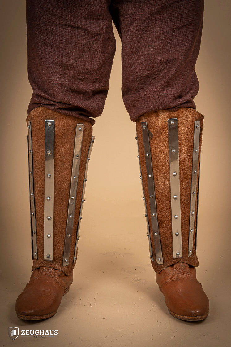 Brown suede leather greaves with riveted metal bands, showcasing a unique three-piece design for shin protection.