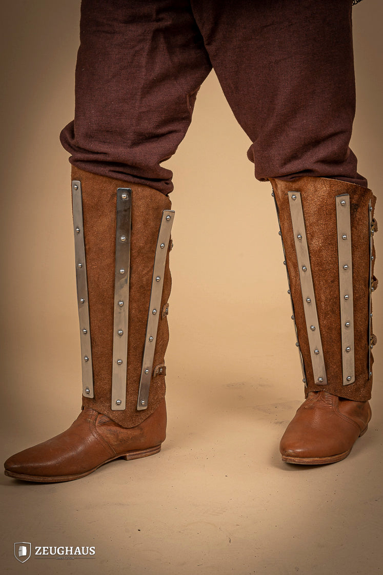 Brown suede leather greaves with riveted metal bands, showcasing a unique three-piece design for shin protection.