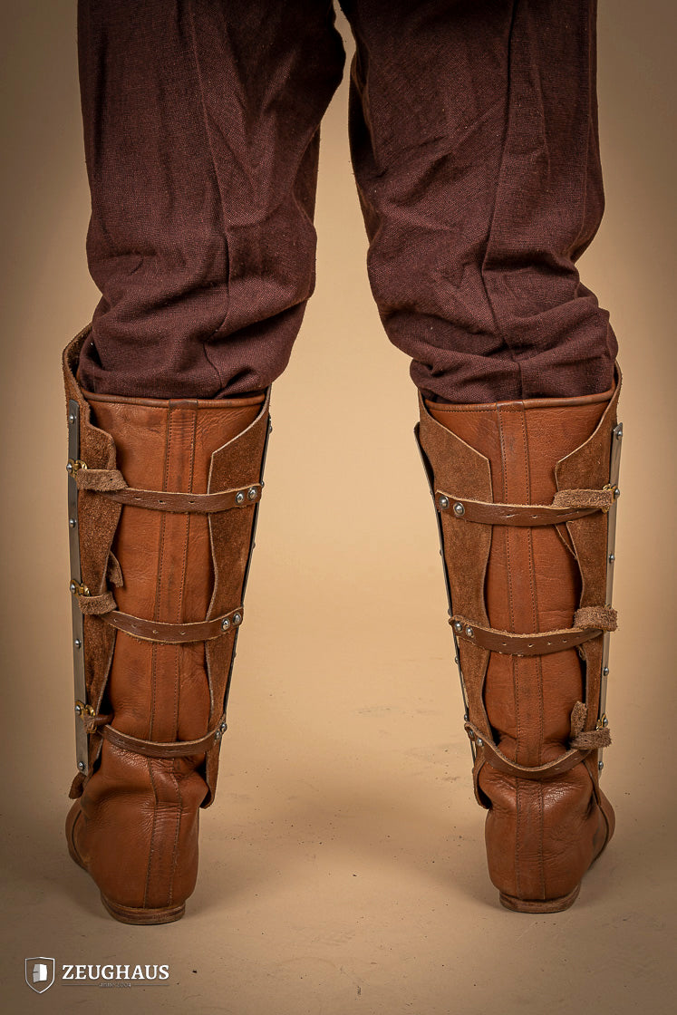Brown suede leather greaves with riveted metal bands, showcasing a unique three-piece design for shin protection.