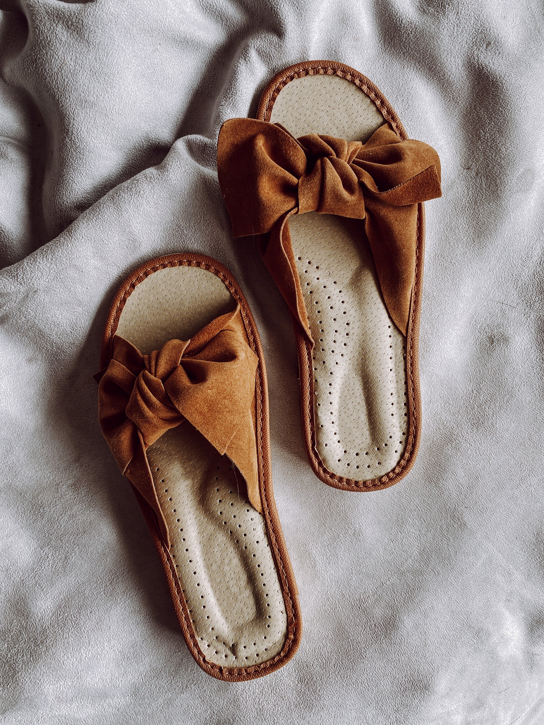 Brown suede slippers featuring a stylish ribbon front and cushioned insole, perfect for warm weather.