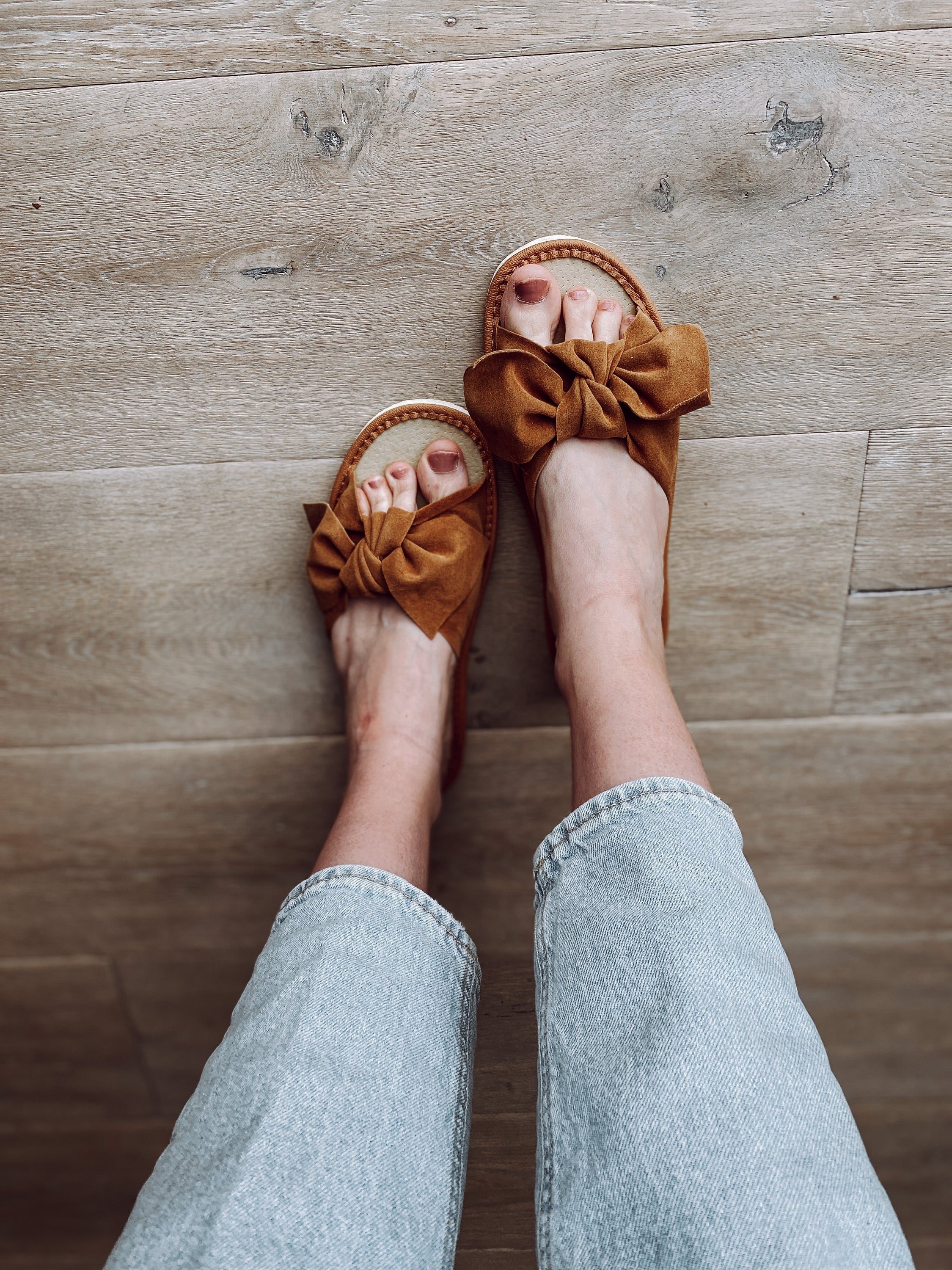 Brown suede slippers featuring a stylish ribbon front and cushioned insole, perfect for warm weather.