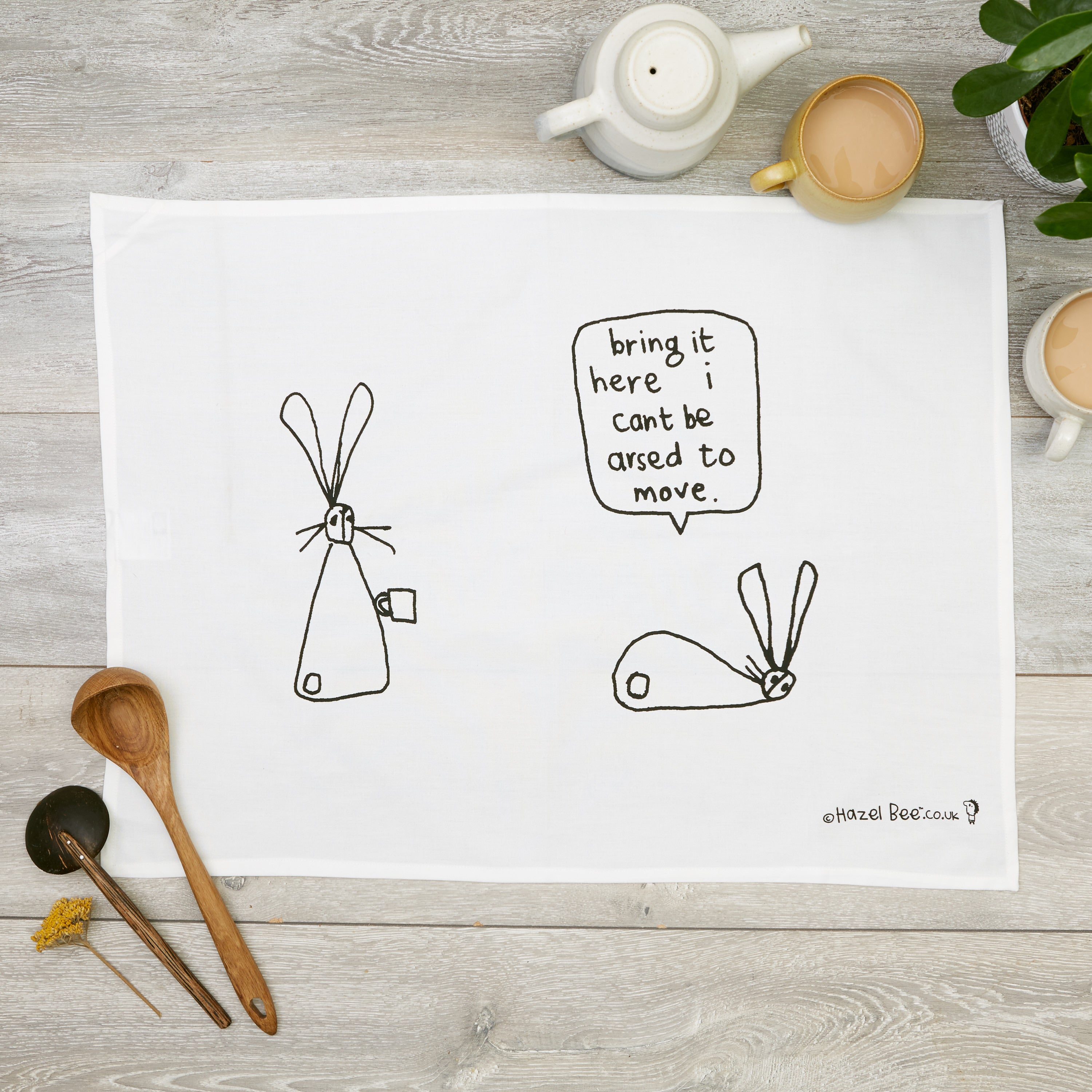 A stylish Can't Be Arsed Tea Towel made from organic cotton, featuring a humorous design in black ink, with a hanging loop for easy storage.