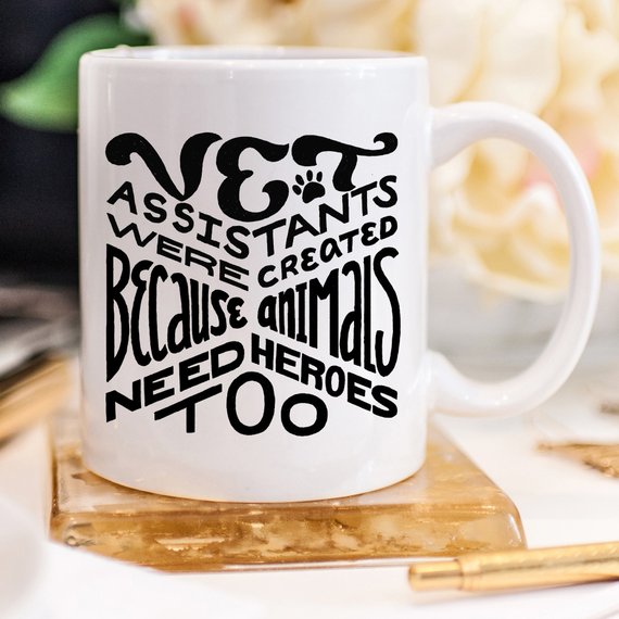 A humorous 11oz coffee mug featuring the phrase 'Vet Assistants Were Created Because Animals Need Heroes Too', designed for animal lovers.