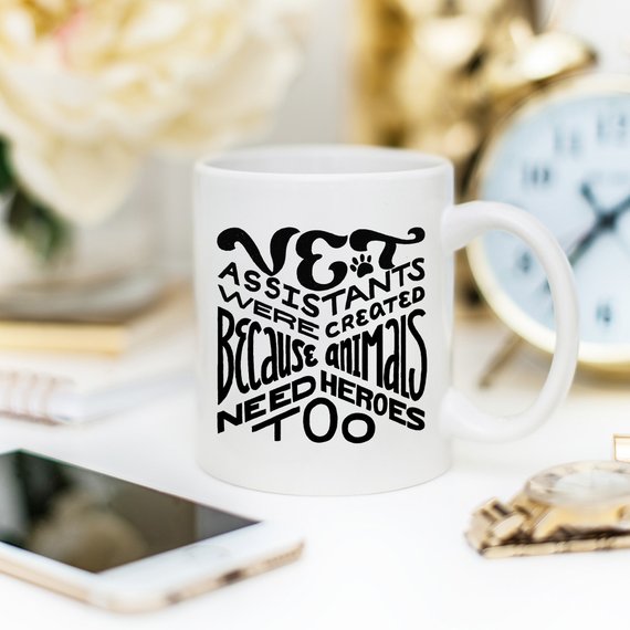 A humorous 11oz coffee mug featuring the phrase 'Vet Assistants Were Created Because Animals Need Heroes Too', designed for animal lovers.