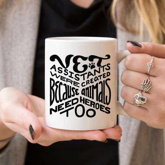 A humorous 11oz coffee mug featuring the phrase 'Vet Assistants Were Created Because Animals Need Heroes Too', designed for animal lovers.