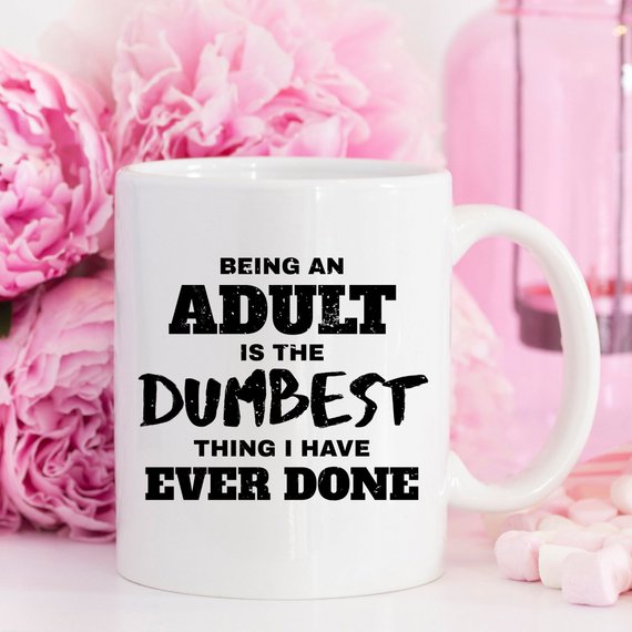 A humorous coffee mug with the phrase 'Being An Adult Is The Dumbest Thing I Have Ever Done' printed on it, showcasing a fun design.