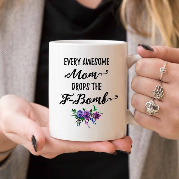A white ceramic mug with the phrase 'Every Awesome Mom Drops the F Bomb' printed in vibrant colors on both sides, perfect for coffee lovers.