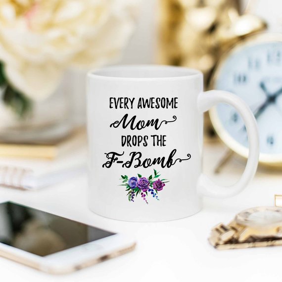 A white ceramic mug with the phrase 'Every Awesome Mom Drops the F Bomb' printed in vibrant colors on both sides, perfect for coffee lovers.