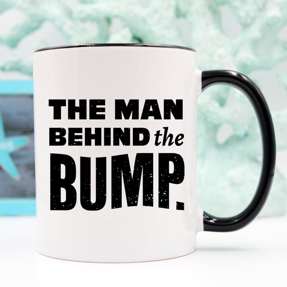 A humorous coffee mug featuring the phrase 'The Man Behind The Bump', crafted from high-grade ceramic, perfect for gifting.