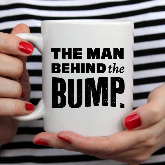 A humorous coffee mug featuring the phrase 'The Man Behind The Bump', crafted from high-grade ceramic, perfect for gifting.