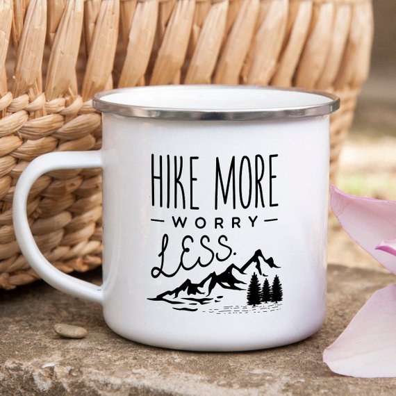 A white enamel mug with a stainless steel rim, featuring a vibrant wanderlust design printed on both sides, perfect for hiking and outdoor adventures.