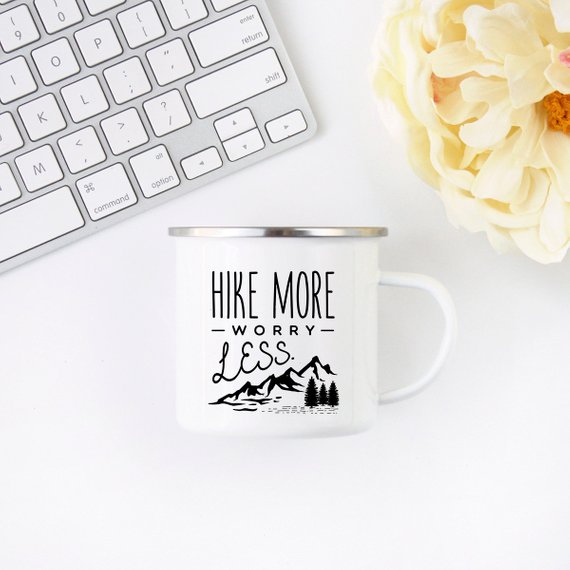 A white enamel mug with a stainless steel rim, featuring a vibrant wanderlust design printed on both sides, perfect for hiking and outdoor adventures.