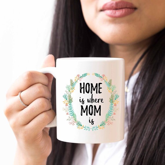 A white ceramic mug with the phrase 'Home Is Where Mom Is' printed in vibrant colors on both sides, showcasing a heartfelt design.