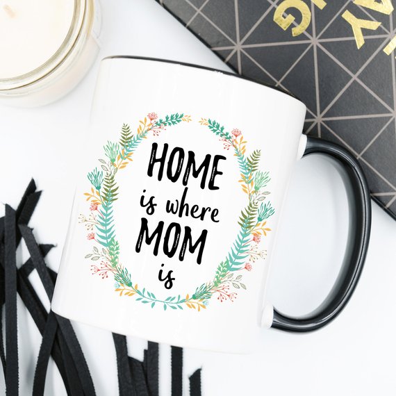 A white ceramic mug with the phrase 'Home Is Where Mom Is' printed in vibrant colors on both sides, showcasing a heartfelt design.
