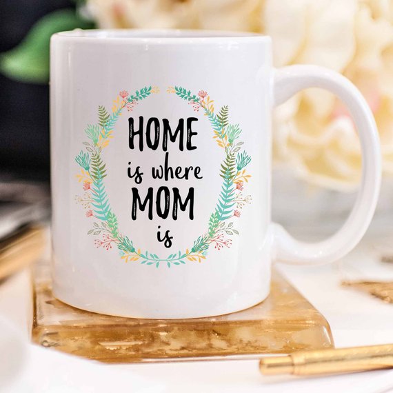 A white ceramic mug with the phrase 'Home Is Where Mom Is' printed in vibrant colors on both sides, showcasing a heartfelt design.