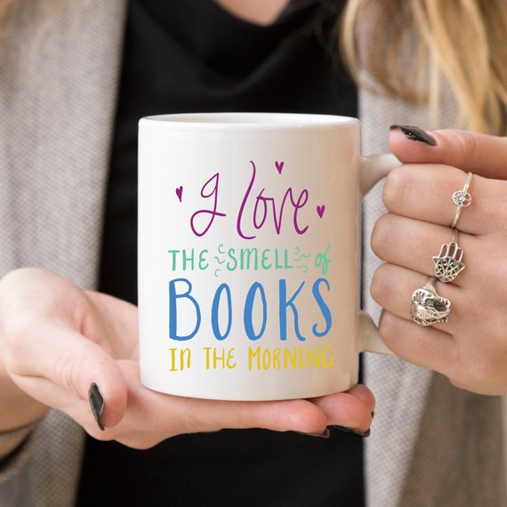 A humorous coffee mug featuring the phrase 'I Love The Smell Of Books In The Morning', designed for book lovers and coffee enthusiasts.