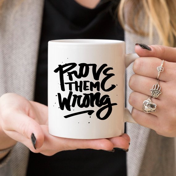 A white ceramic coffee mug with the phrase 'Prove Them Wrong' printed in bold letters, showcasing a motivational and humorous design.