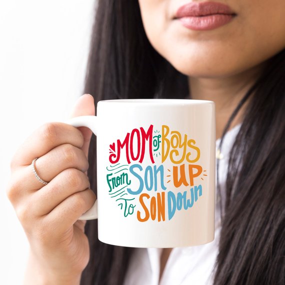 A humorous coffee mug designed for moms of boys, featuring the phrase 'Mom Of Boys, From Son Up To Son Down' in a playful font.