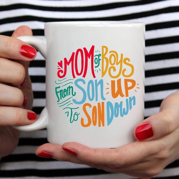 A humorous coffee mug designed for moms of boys, featuring the phrase 'Mom Of Boys, From Son Up To Son Down' in a playful font.