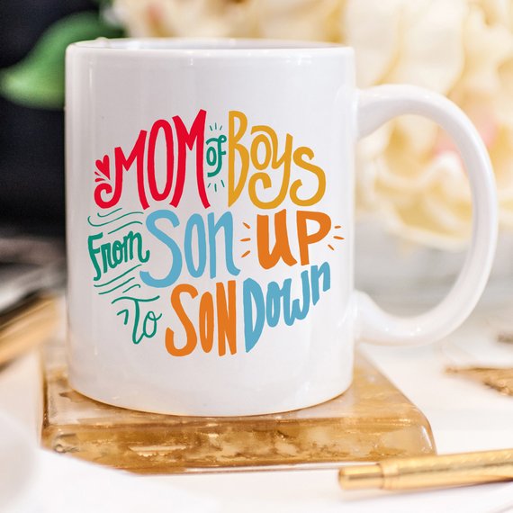 A humorous coffee mug designed for moms of boys, featuring the phrase 'Mom Of Boys, From Son Up To Son Down' in a playful font.