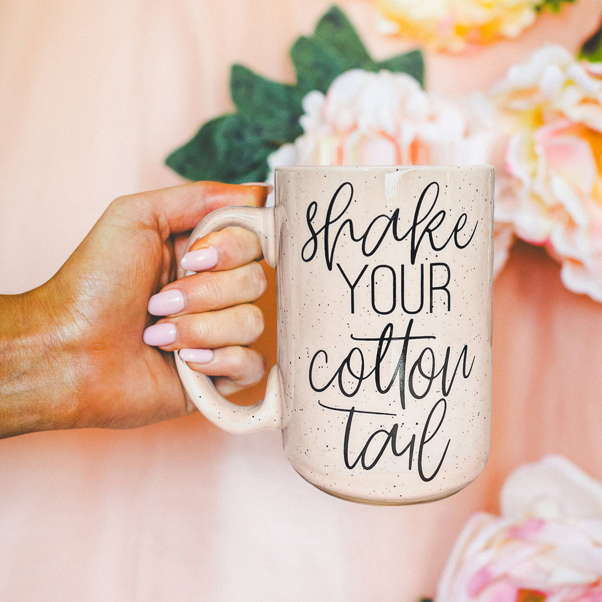 A pastel blue and pink ceramic coffee mug with 'Shake Your Cotton Tail' graphic, showcasing a fun Easter design.