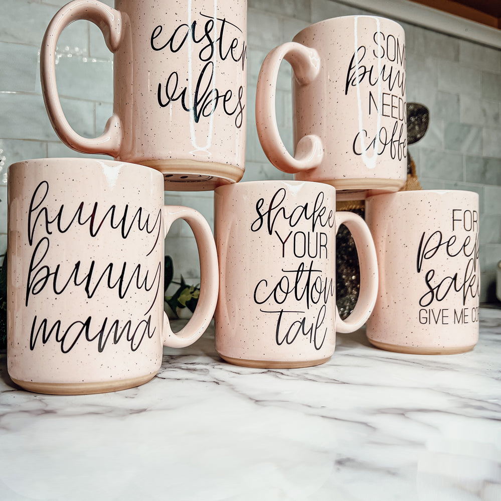 A pastel blue and pink ceramic coffee mug with 'Shake Your Cotton Tail' graphic, showcasing a fun Easter design.
