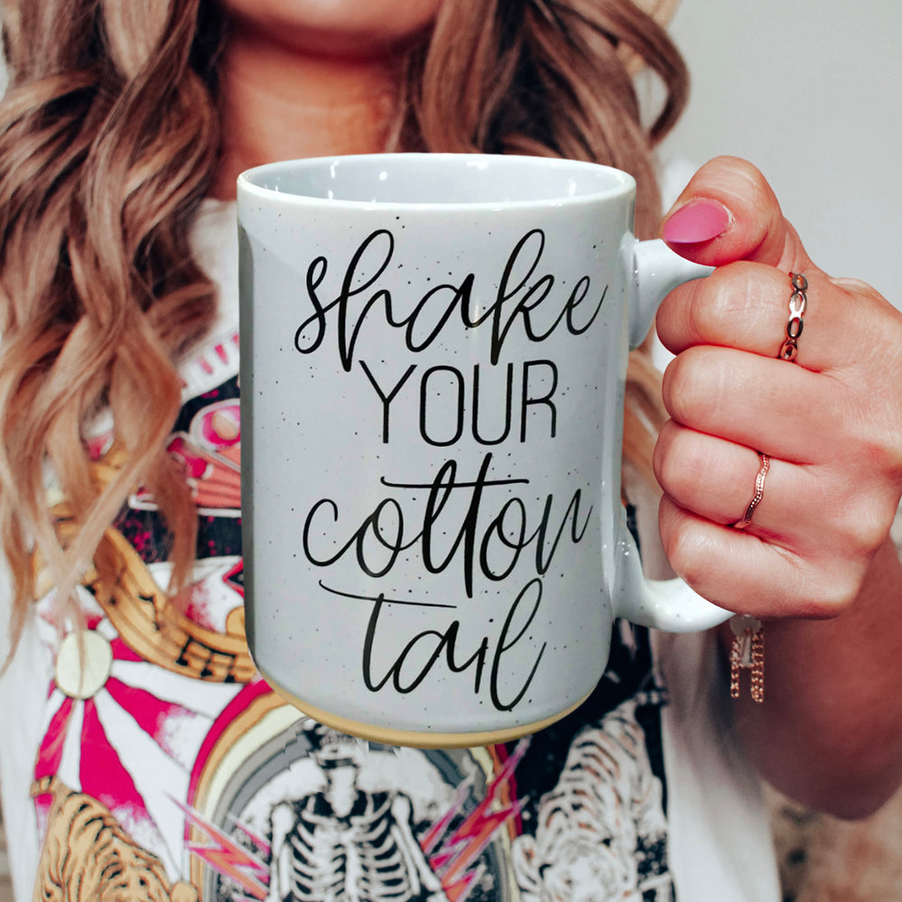 A pastel blue and pink ceramic coffee mug with 'Shake Your Cotton Tail' graphic, showcasing a fun Easter design.