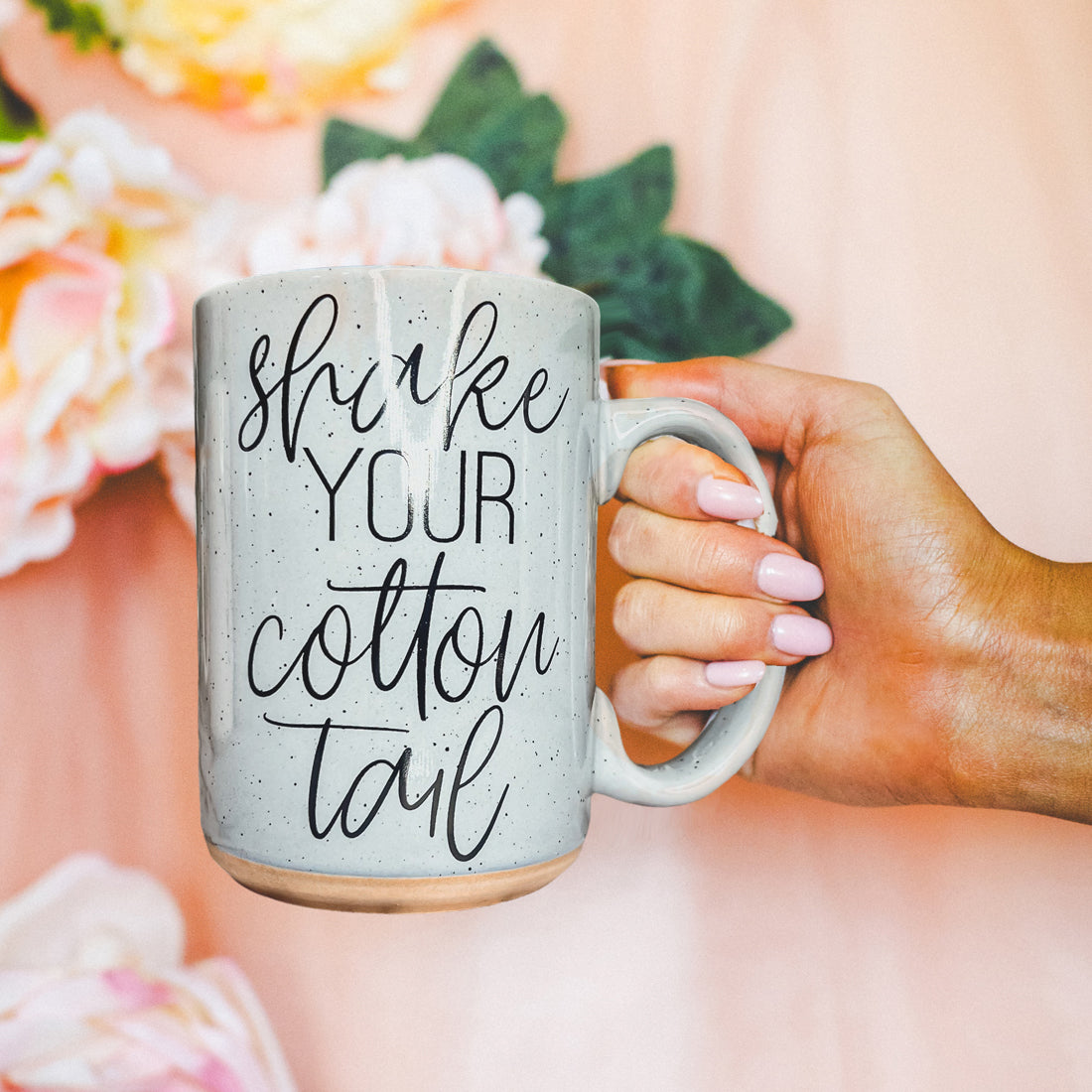 A pastel blue and pink ceramic coffee mug with 'Shake Your Cotton Tail' graphic, showcasing a fun Easter design.