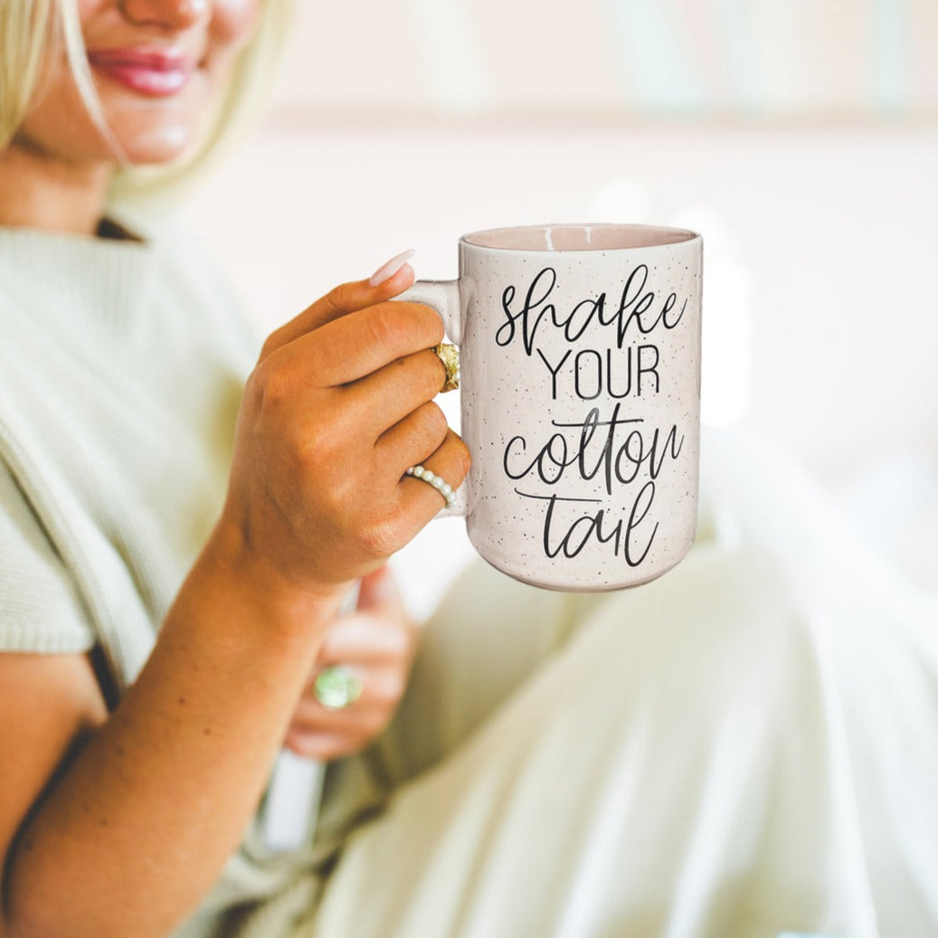 A pastel blue and pink ceramic coffee mug with 'Shake Your Cotton Tail' graphic, showcasing a fun Easter design.