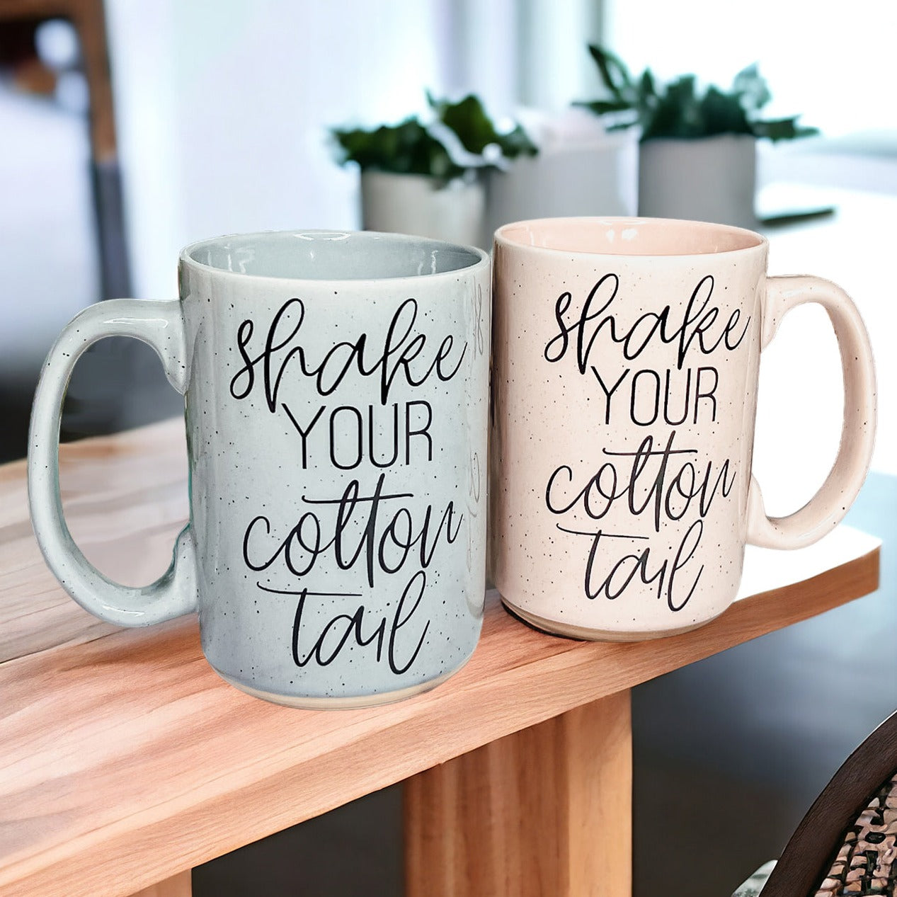 A pastel blue and pink ceramic coffee mug with 'Shake Your Cotton Tail' graphic, showcasing a fun Easter design.