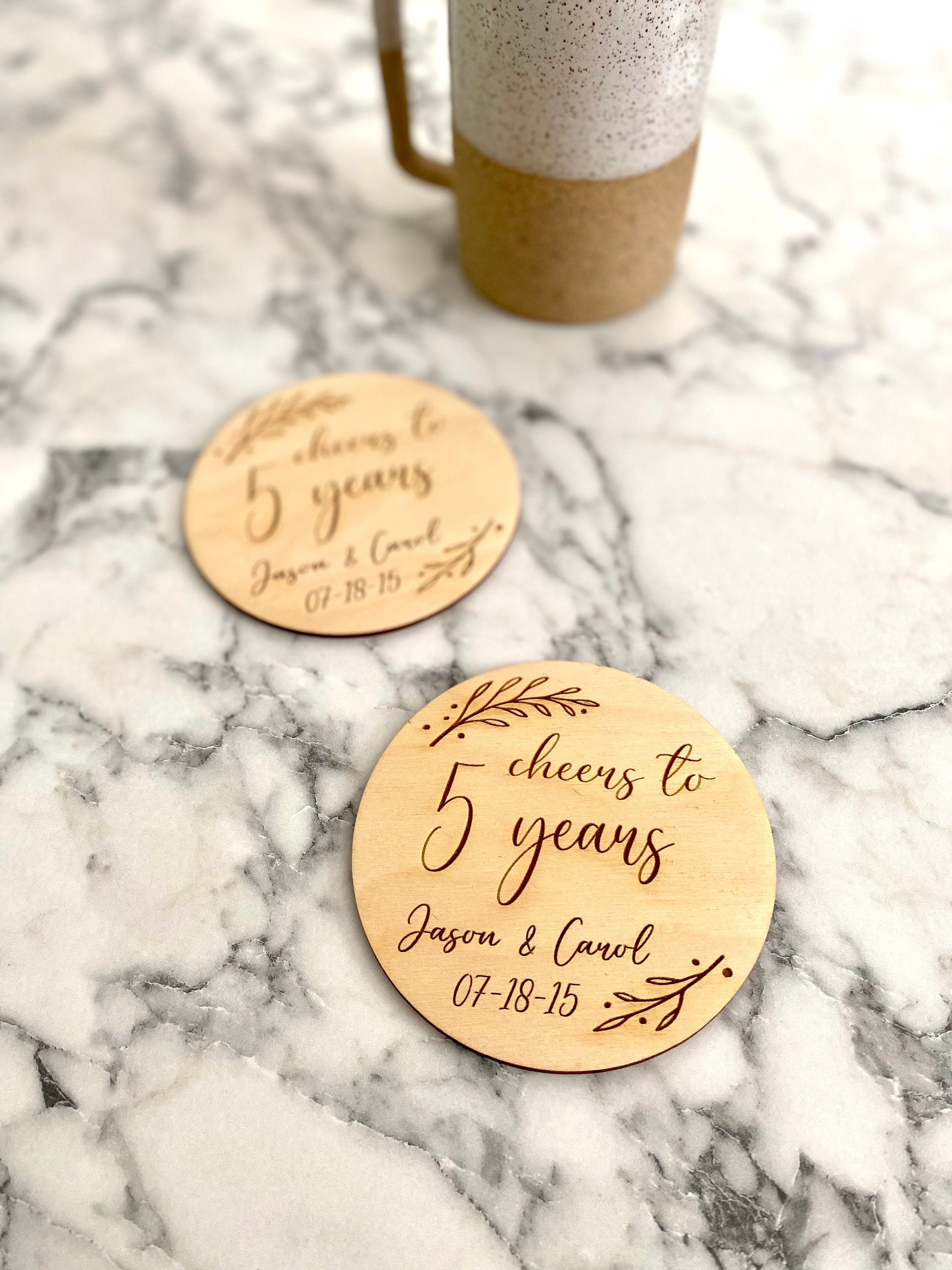 A beautifully crafted 5 Year Anniversary Coaster Set made of Baltic Birch, featuring personalized laser engraving of names and wedding date with an elegant leaf border.