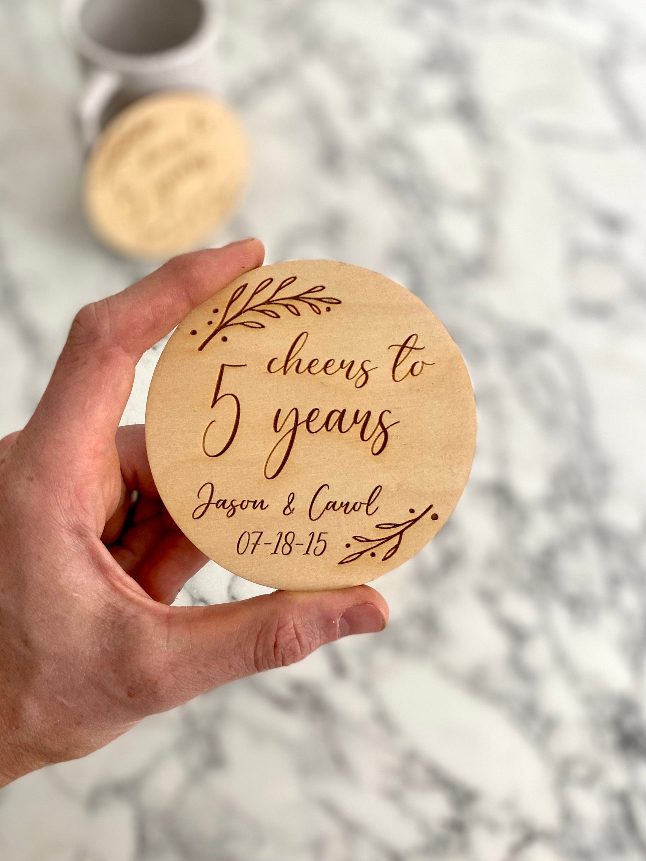 A beautifully crafted 5 Year Anniversary Coaster Set made of Baltic Birch, featuring personalized laser engraving of names and wedding date with an elegant leaf border.