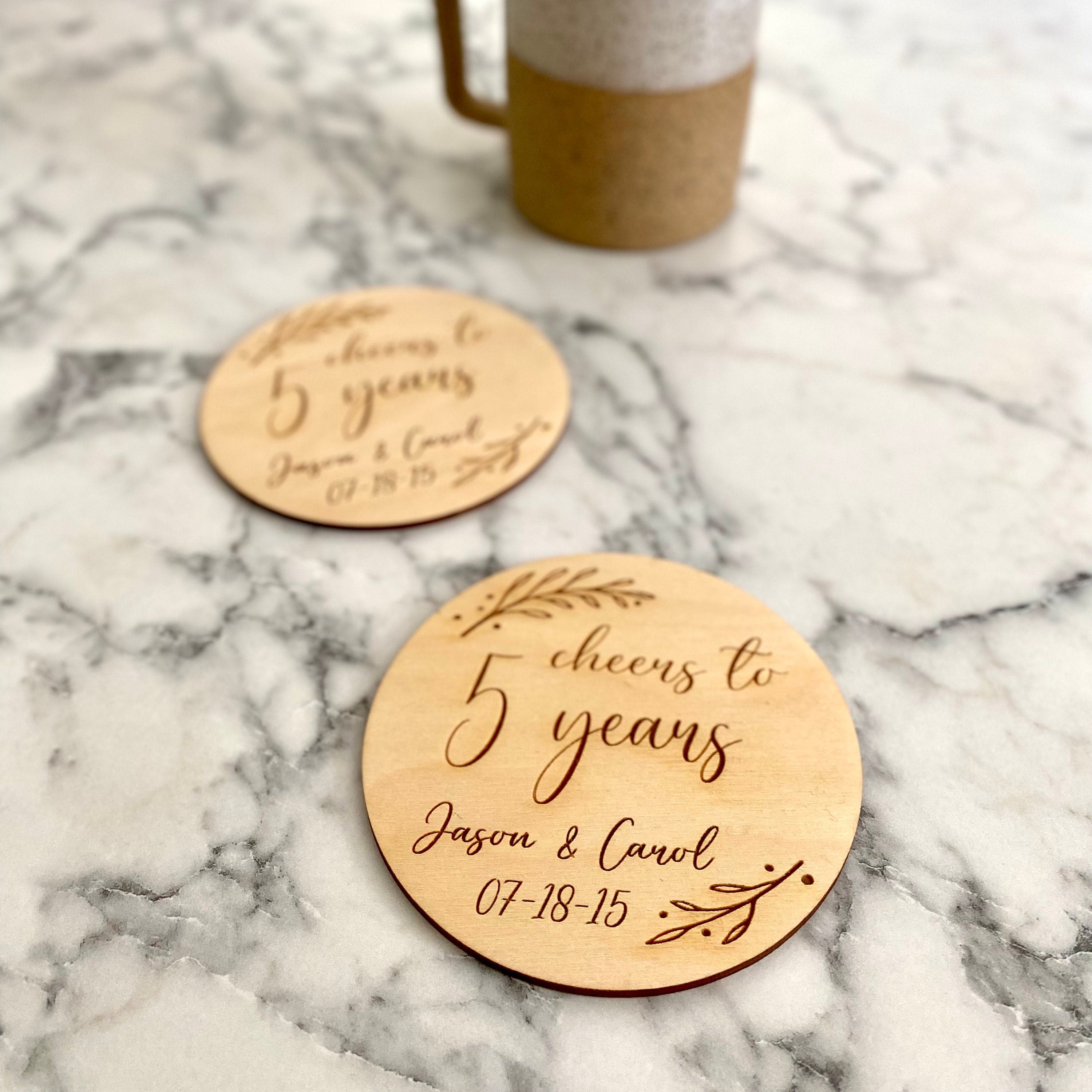 A beautifully crafted 5 Year Anniversary Coaster Set made of Baltic Birch, featuring personalized laser engraving of names and wedding date with an elegant leaf border.