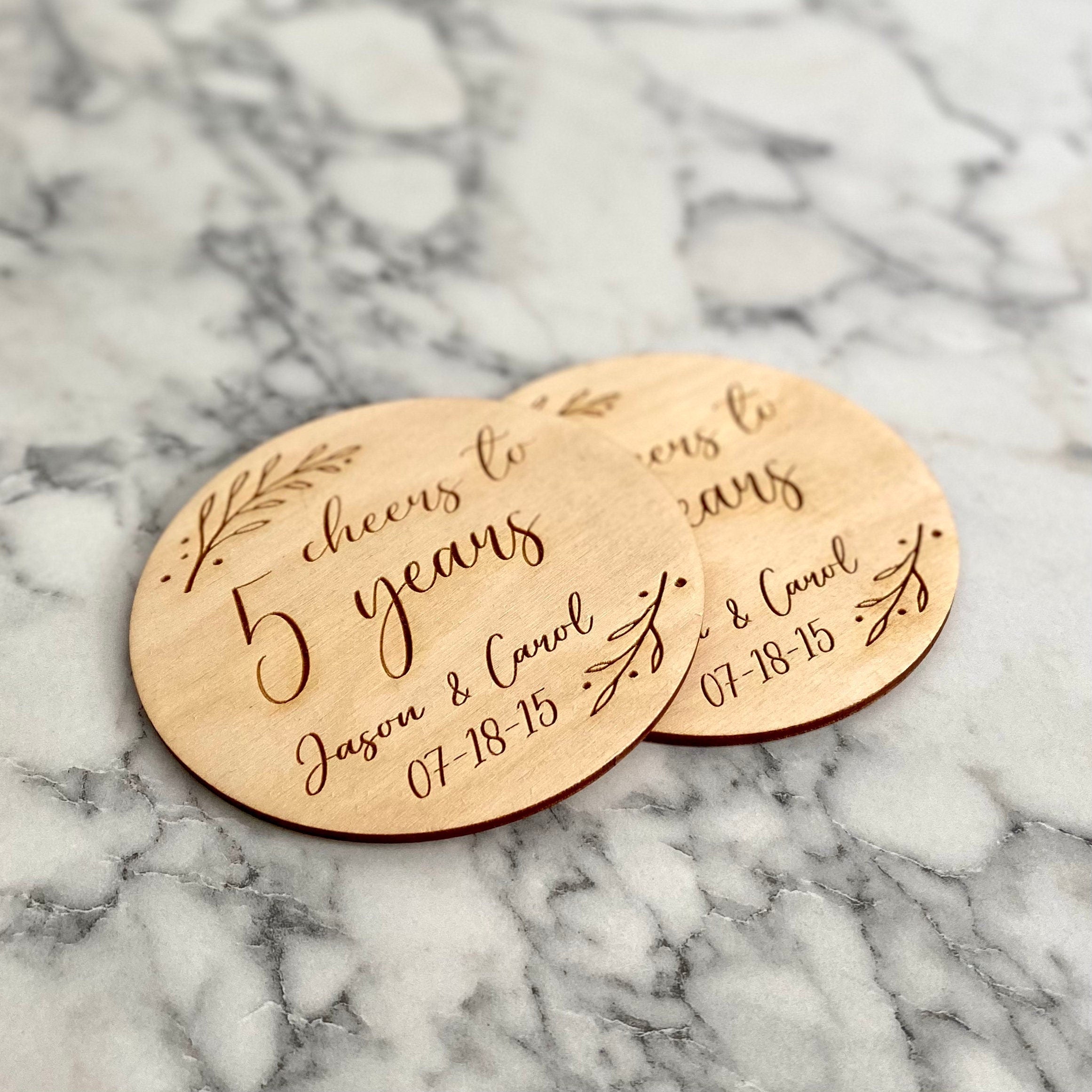 A beautifully crafted 5 Year Anniversary Coaster Set made of Baltic Birch, featuring personalized laser engraving of names and wedding date with an elegant leaf border.