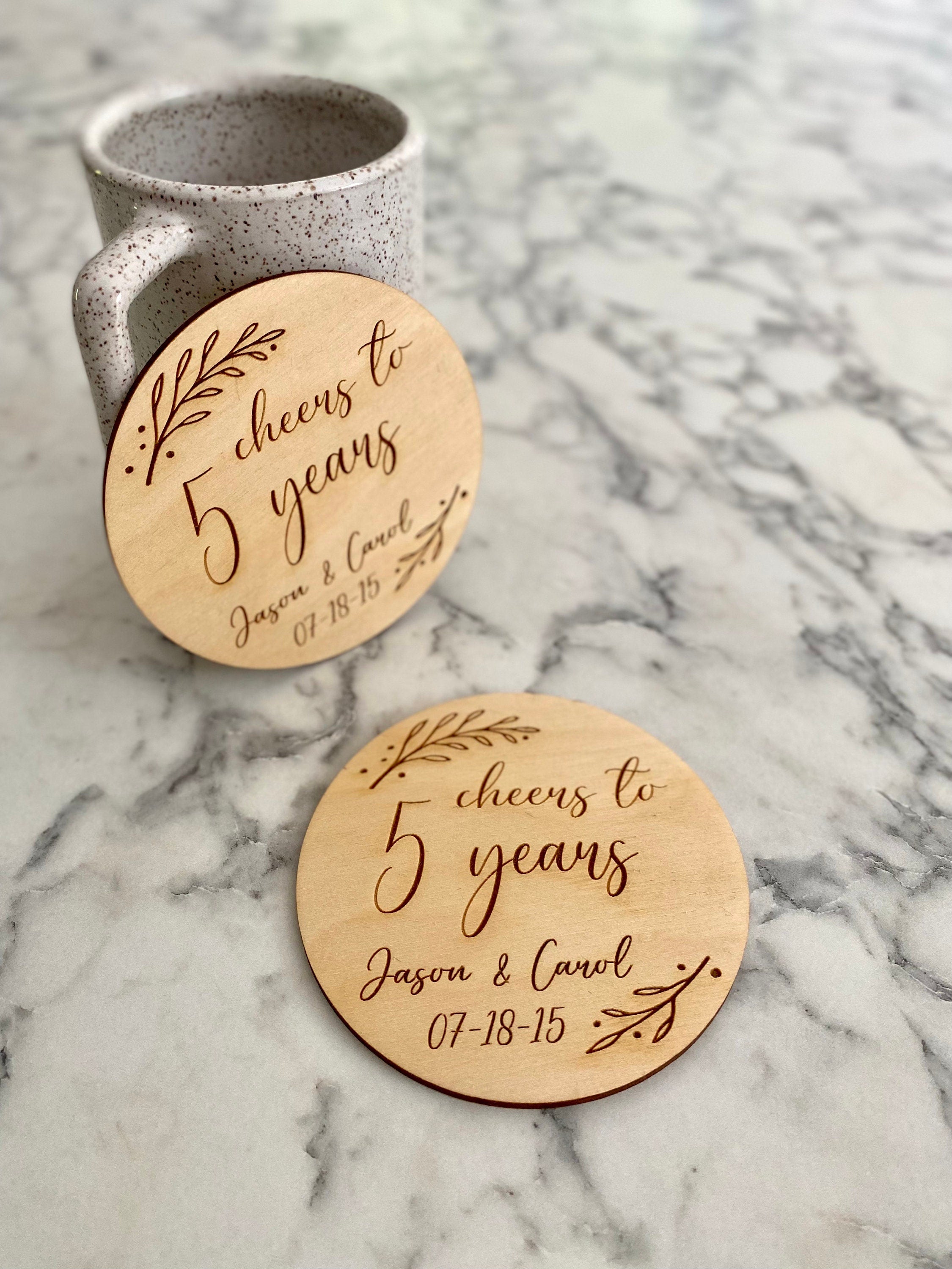 A beautifully crafted 5 Year Anniversary Coaster Set made of Baltic Birch, featuring personalized laser engraving of names and wedding date with an elegant leaf border.