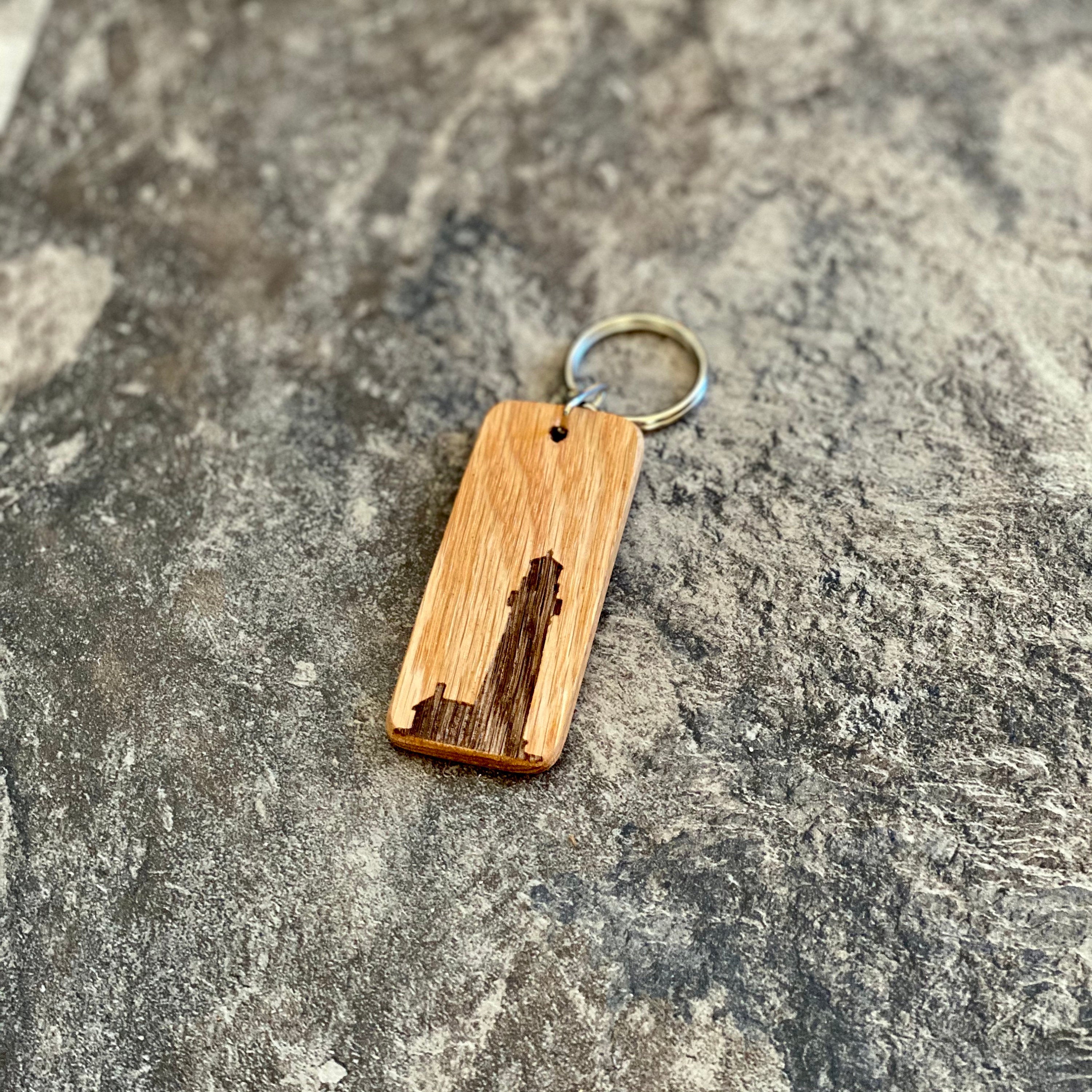 A rustic wooden keychain featuring a laser engraved lighthouse silhouette, showcasing its natural oak finish and custom engraving option.